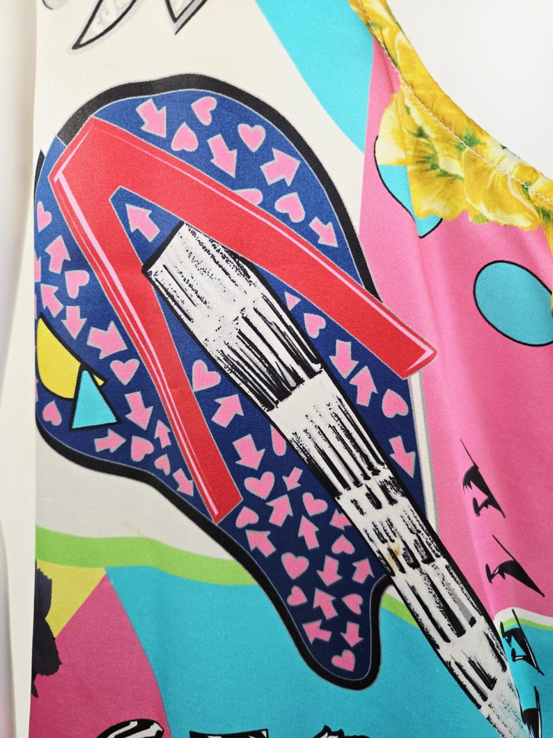 Puede incluir: Una prenda sin mangas con un estampado gr&aacute;fico vibrante y multicolor. El dise&ntilde;o incluye una letra A roja grande y estilizada sobre un fondo azul oscuro lleno de peque&ntilde;os corazones y flechas rosas, junto con motivos florales amarillos.