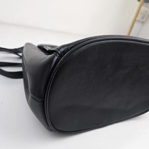 Pu&ograve; includere: Una borsa in pelle nera con fondo arrotondato e manico superiore. La borsa ha una consistenza liscia e un design semplice e classico. Le cuciture sono visibili lungo i bordi, aggiungendo dettagli alla borsa.