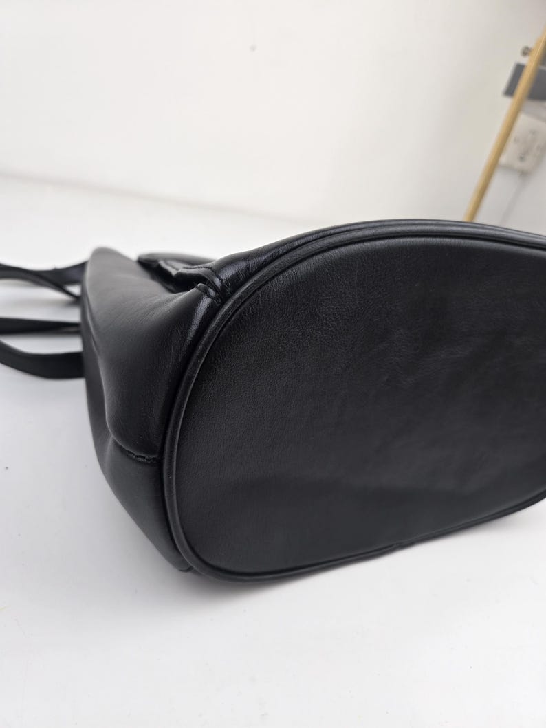Pu&ograve; includere: Una borsa in pelle nera con fondo arrotondato e manico superiore. La borsa ha una consistenza liscia e un design semplice e classico. Le cuciture sono visibili lungo i bordi, aggiungendo dettagli alla borsa.