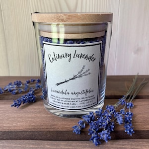 May include: A clear glass jar filled with dried purple lavender buds, topped with a light-colored bamboo lid. The white label reads Culinary Lavender, Lavandula angustifolia, English Lavender cultivated without chemicals in Michigan, .7 oz. (20 g.).