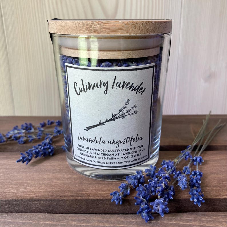 May include: A clear glass jar filled with dried purple lavender buds, topped with a light-colored bamboo lid. The white label reads Culinary Lavender, Lavandula angustifolia, English Lavender cultivated without chemicals in Michigan, .7 oz. (20 g.).