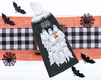 May include: A black kitchen towel with a white crocheted top. The towel features a black and white checked pattern and a graphic of a dog surrounded by ghosts. The text "Boo!" is printed on the towel.