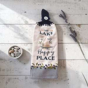 May include: A hanging kitchen towel with a dark blue crocheted top and a white button. The cream-colored fabric features a sailboat illustration, the text THE LAKE is my Happy PLACE, and a bottom border of blue berries and navy vertical stripes.