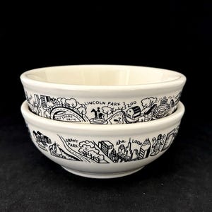 Puede incluir: Dos cuencos de cerámica blancos apilados. Cada cuenco tiene un diseño ilustrado en blanco y negro de los monumentos de una ciudad, incluyendo texto que dice "Lincoln Park Zoo" y "Grant Park".