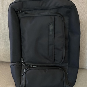 May include: A black rectangular backpack featuring multiple zippered compartments and pockets. The front displays the eBags brand name embossed vertically on a central pocket. The bag is constructed from a durable, textured fabric with black zippers.