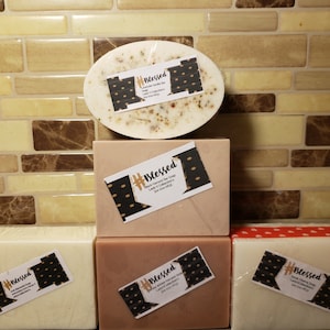 May include: Four bars of handmade soap with a white base and a brown and black label that says "#Blessed" with a small graphic of the state of Missouri. The soap bars are stacked on top of each other on a brown tiled surface.