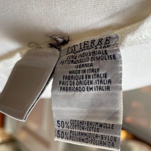 May include: Close-up of a white fabric tag with text in multiple languages. The tag reads "ITIERRE" and "MADE IN ITALY". The tag also lists the fabric composition as 50% cotton and 50% polyamide.