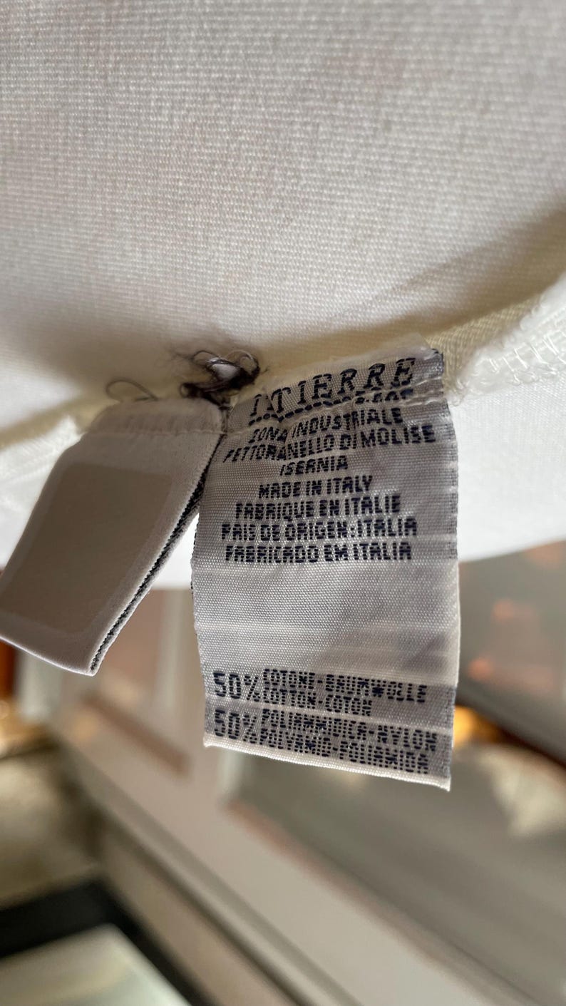 May include: Close-up of a white fabric tag with text in multiple languages. The tag reads "ITIERRE" and "MADE IN ITALY". The tag also lists the fabric composition as 50% cotton and 50% polyamide.