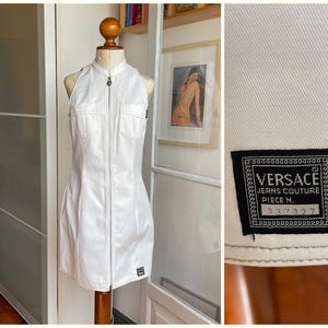 May include: White halter-neck dress with a zip-up front and two front pockets. The dress is displayed on a mannequin. A black label with the Versace Jeans Couture logo and the number 337327 is visible.