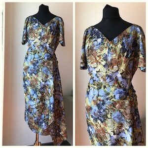 May include: A vintage wrap dress with a blue, brown, and green floral print. The dress has a V-neckline, short sleeves, and a fitted silhouette.