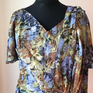 May include: A vintage dress with a V-neckline and short sleeves. The dress is made of a light-weight fabric with a blue, green, and brown abstract floral print.