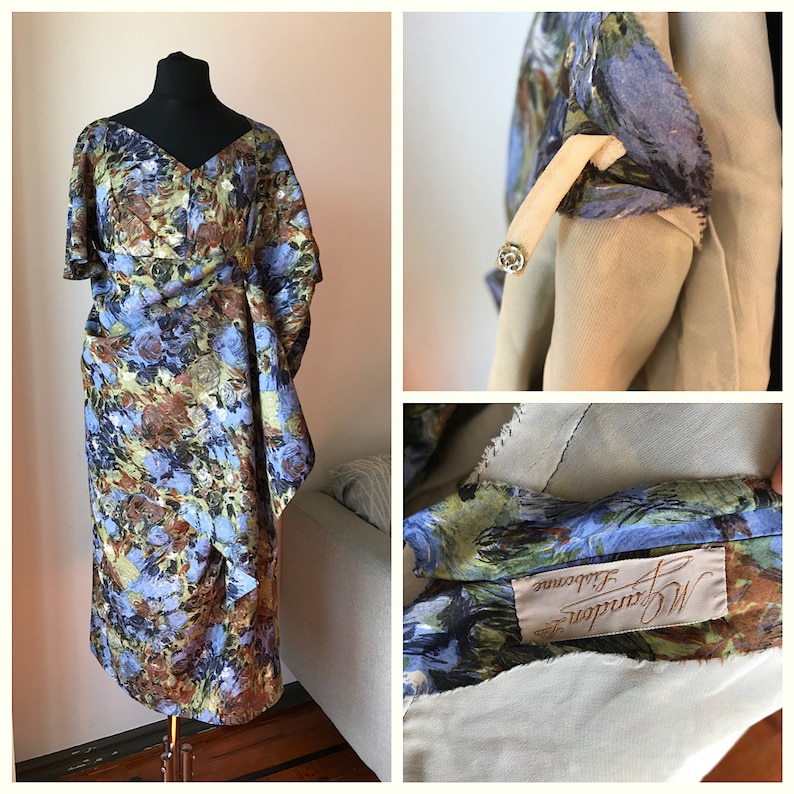 May include: A vintage floral print dress with a V-neckline and short sleeves. The dress has a fitted bodice and a flowing skirt. The dress is made of a lightweight fabric and has a light blue, brown, and green color scheme. The dress has a label that reads "M. Grandeur, Melbourne".