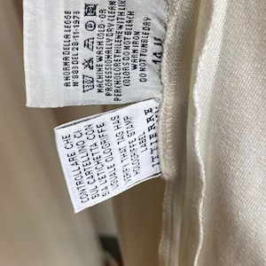 May include: Close-up of a garment tag with washing instructions and the text "A NORMA DELLA LEGGE N'883 DEL 28-11-1973". The tag also includes the text "CONTROLLARE CHE SUL CARTELLINO CI SIA L'ETICHETTA CON UGUALE OLOGRIFFE".