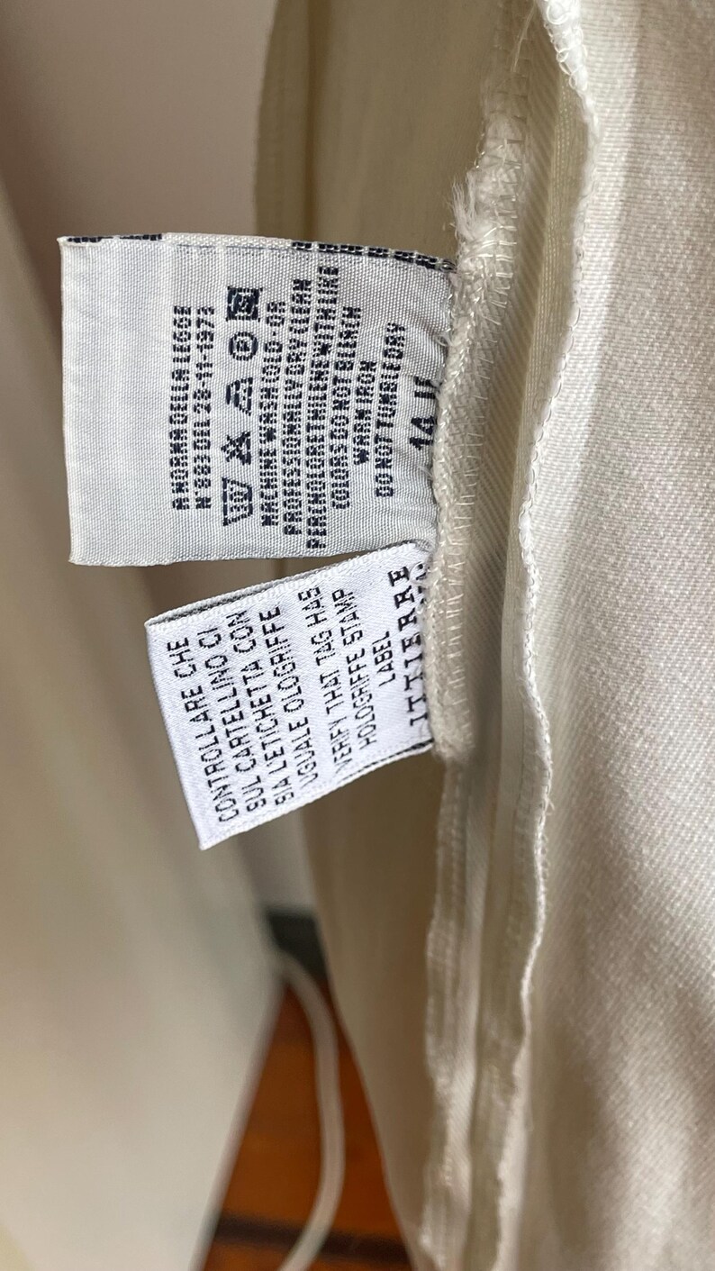 May include: Close-up of a garment tag with washing instructions and the text "A NORMA DELLA LEGGE N'883 DEL 28-11-1973". The tag also includes the text "CONTROLLARE CHE SUL CARTELLINO CI SIA L'ETICHETTA CON UGUALE OLOGRIFFE".