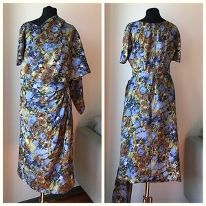 May include: A blue, brown, and green floral print dress with a short sleeve and a fitted bodice. The dress has a draped skirt and a matching scarf.