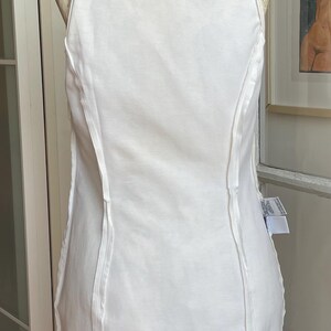 May include: A white sleeveless dress with a high neckline and vertical seams. The dress is displayed on a mannequin. A small black and white Versace label is visible at the neckline.
