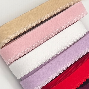 Può includere: Cinque bobine di passamaneria elastica con bordi a festoni. I colori sono beige, rosa, bianco, lavanda e rosso.
