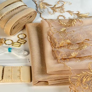 May include: A set of beige and gold fabric and trim for sewing projects. The set includes lace, tulle, elastic, and bra straps.