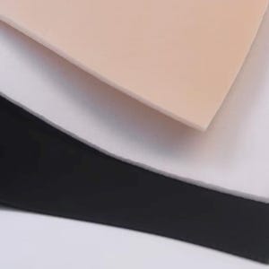 May include: A stack of three rectangular sheets of material layered on top of each other. The top sheet is a light beige color, the middle sheet is white, and the bottom sheet is black. Each sheet has a smooth, flat, and uniform surface.