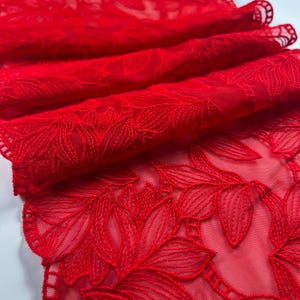 Puede incluir: Primer plano de una vibrante tela de encaje rojo con un patrón de hojas florales. El delicado bordado crea un efecto texturizado, con la tela doblada para mostrar profundidad y detalles. Ideal para manualidades o ropa.