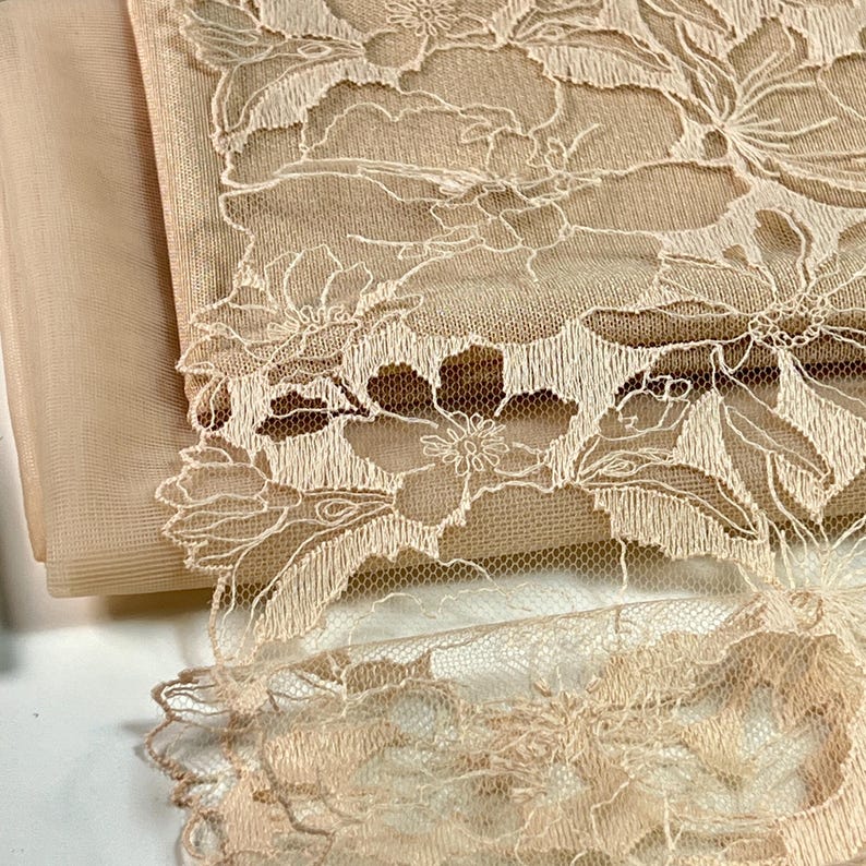 Puede incluir: Tela de encaje floral beige con un patr&oacute;n delicado. El encaje es transparente y tiene una textura suave y fluida.