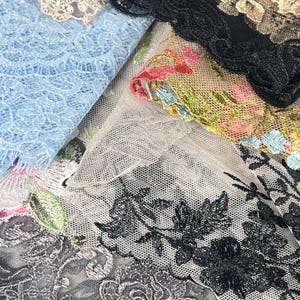 May include: Close-up of various lace fabrics in shades of blue, black, and floral patterns. The lace features intricate designs and textures, suitable for sewing and crafting projects. The fabrics include embroidered details and delicate edges.