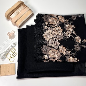 Könnte beinhalten: Ein Set aus schwarzem Stoff, Spitze und Netz mit goldener Stickerei. Das Set enthält zwei Stücke schwarzen Stoffes, ein Stück schwarze Spitze mit goldener Stickerei und ein Stück schwarzes Netz. Das Set enthält außerdem ein Stück beigefarbenen Stoffes mit BH-Haken, ein Stück beigefarbenes Gummiband mit gewelltem Rand, ein Stück beigefarbenes Band, ein Stück weißes Band, ein Stück weißes Garn, ein Stück goldenes Garn, zwei goldene Ringe und einen Satz goldener BH-Haken.