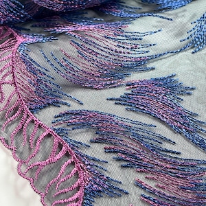 May include: Close-up of a fabric with a feather-like design. The fabric features a mesh base with embroidered details in shades of blue, purple, and pink. The edge of the fabric has a scalloped, embroidered trim in pink.