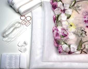 May include: A set of white fabric and lace trim for a DIY lingerie project. The set includes two pieces of white fabric, a piece of white lace trim, a piece of white ribbon, two metal rings, a piece of clear elastic, and a bra hook and eye closure.