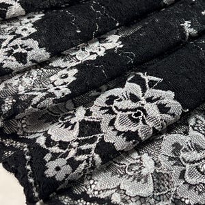 Könnte beinhalten: Schwarzer Spitzenstoff mit silbernem Blumenmuster. Die Spitze ist zart und filigran, mit einer weichen, fließenden Textur.