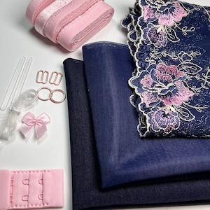 May include: A set of navy blue fabric, pink ribbon, and hardware for making a bra. The fabric includes a piece of mesh and a piece of solid fabric. The hardware includes two metal rings, two metal clasps, and a pink plastic bra strap adjuster.