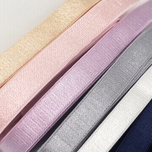 Op de afbeelding: Assortiment van zes elastiekjes in verschillende kleuren, waaronder goud, roze, lavendel, grijs, wit en marineblauw. De elastiekjes hebben een textuur en een glinsterende afwerking.