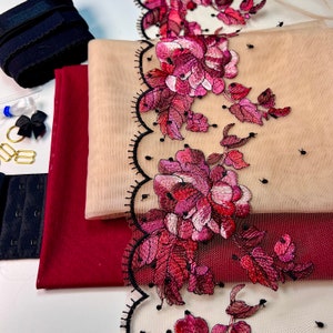 Könnte beinhalten: Nahaufnahme eines schwarzen und burgunderfarbenen Stoffes mit einer floralen Spitzenborte. Die Spitze ist mit rosa und roten Blumen und Blättern bestickt. Der Stoff ist geschichtet und hat eine durchscheinende Textur.