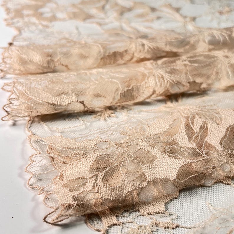 Puede incluir: Tela de encaje beige con un patr&oacute;n floral. El encaje tiene un borde festoneado.