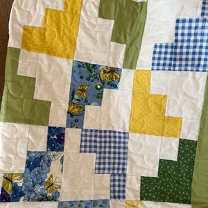 May include: A white quilt with a patchwork design featuring yellow, green, blue, and white fabric squares. The quilt is quilted with a pattern of small circles.