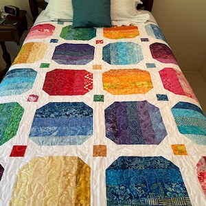 May include: A twin-sized quilt featuring a repeating pattern of octagonal blocks in various rainbow colors, including red, orange, yellow, green, blue, and purple. The blocks are separated by white sashing and small, multi-colored square cornerstones.