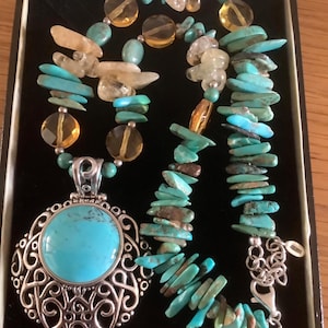 Peut inclure: Un collier de pierres précieuses en turquoise et citrine avec un grand pendentif en turquoise. Le pendentif est serti dans un cadre en filigrane argenté. Le collier présente une variété de perles et d'éclats de turquoise et de citrine.