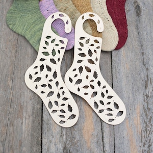 Può includere: Sei paia di calze a maglia esposte su blocca-calze in legno con un motivo a foglie. Le calze sono di vari colori, tra cui verde, viola, beige e rosso.