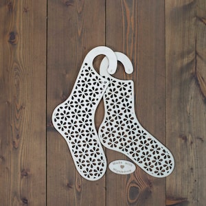 May include: Two white wooden sock-shaped organizers with a floral cutout design. The organizers have a hook at the top and a small oval tag that reads "Made with ♥ Mlynjedrow".