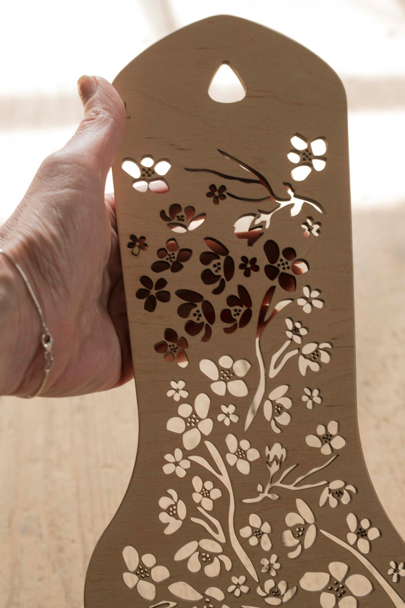 May include: A wooden cutout of a floral design with a delicate pattern of flowers and branches. The cutout is light brown and has a smooth finish.