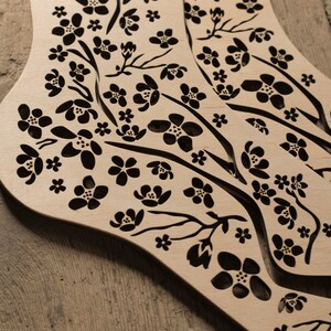 May include: A pair of wooden sock-shaped ornaments with a delicate floral design cut out. The design features small black flowers and branches on a light brown background.