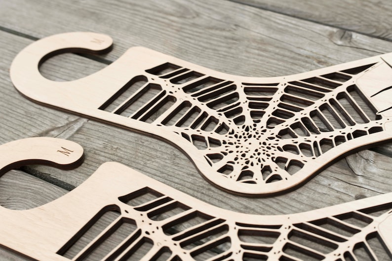 K&ouml;nnte beinhalten: Zwei h&ouml;lzerne Socken-Trockenst&auml;nder mit einem Spinnennetz-Design. Die St&auml;nder haben oben einen Haken zum Aufh&auml;ngen.
