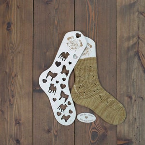 May include: A pair of tan socks and a white sock form with pug dog cutouts and heart shapes. The sock form has a pug face at the top. The socks and forms are on a dark brown wooden surface. A small sticker says "Made with Mlynjedrow".
