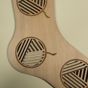 May include: A wooden sock-shaped ornament with three cut-out circles. Each circle has a geometric pattern of lines and a small stem extending from the bottom.