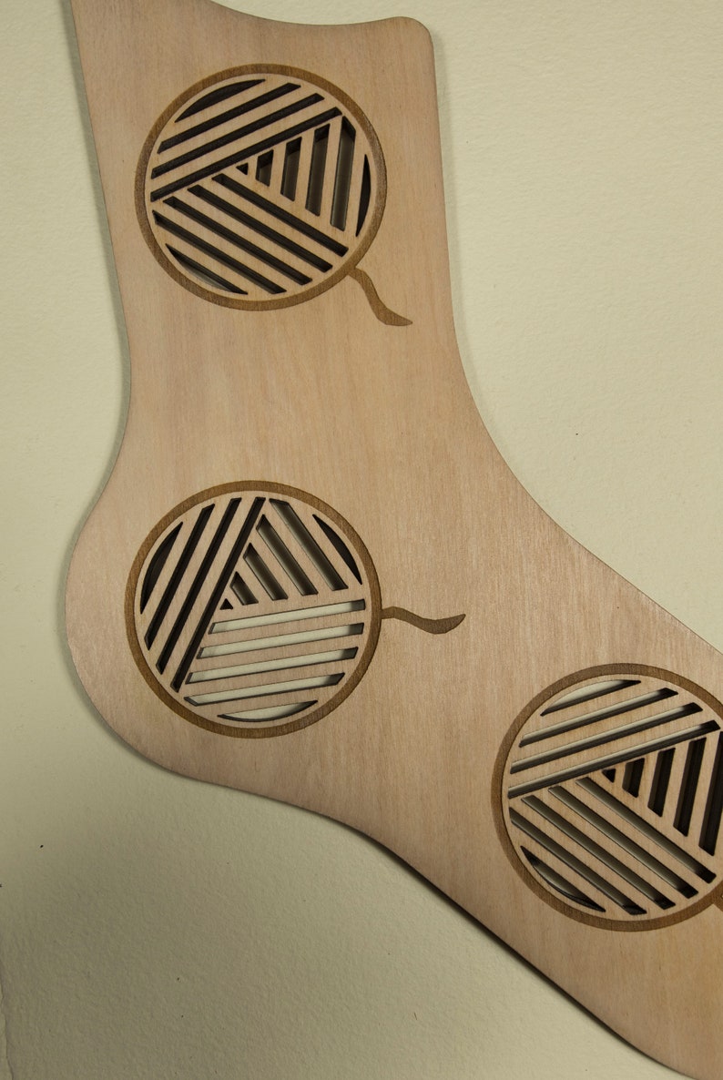 May include: A wooden sock-shaped ornament with three cut-out circles. Each circle has a geometric pattern of lines and a small stem extending from the bottom.