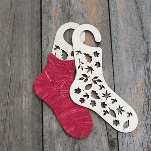 May include: Two wooden sock blockers with leaf cutouts, one with a red knitted sock inside.