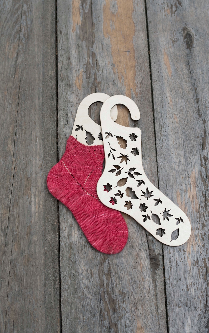 May include: Two wooden sock blockers with leaf cutouts, one with a red knitted sock inside.