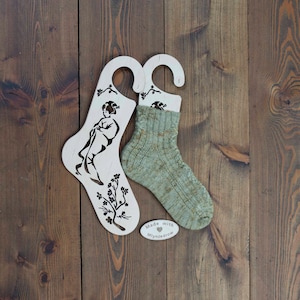 Op de afbeelding: Twee houten sokkenblokkers met een bloemenontwerp en een geishafiguur. Een blokker heeft een groene en bruine sok erop. De sokkenblokker heeft een label met de tekst "Made with ♥ Mynjadrow".