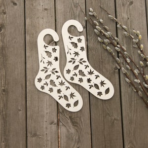 May include: Two white wooden sock drying forms with a leaf pattern. The forms are on a wooden surface.
