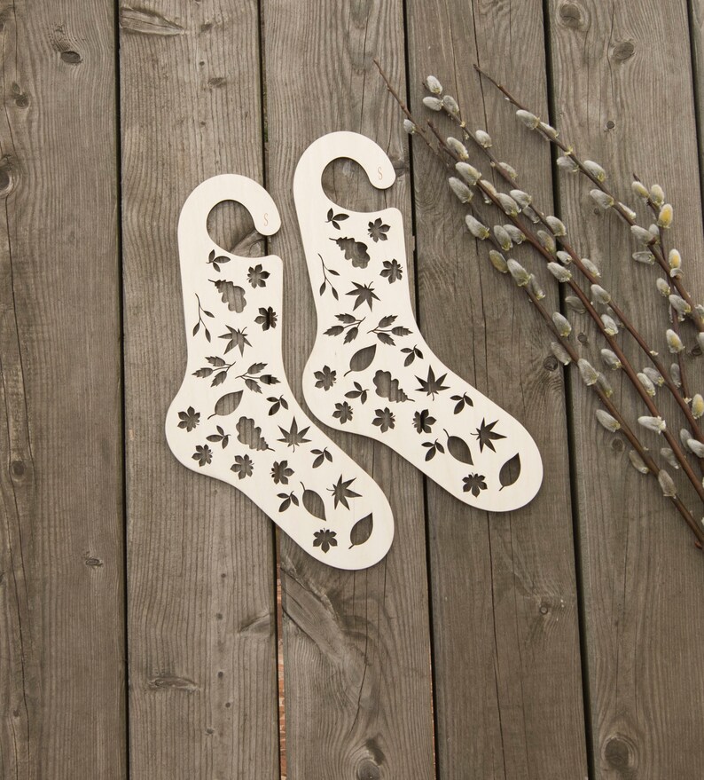 May include: Two white wooden sock drying forms with a leaf pattern. The forms are on a wooden surface.